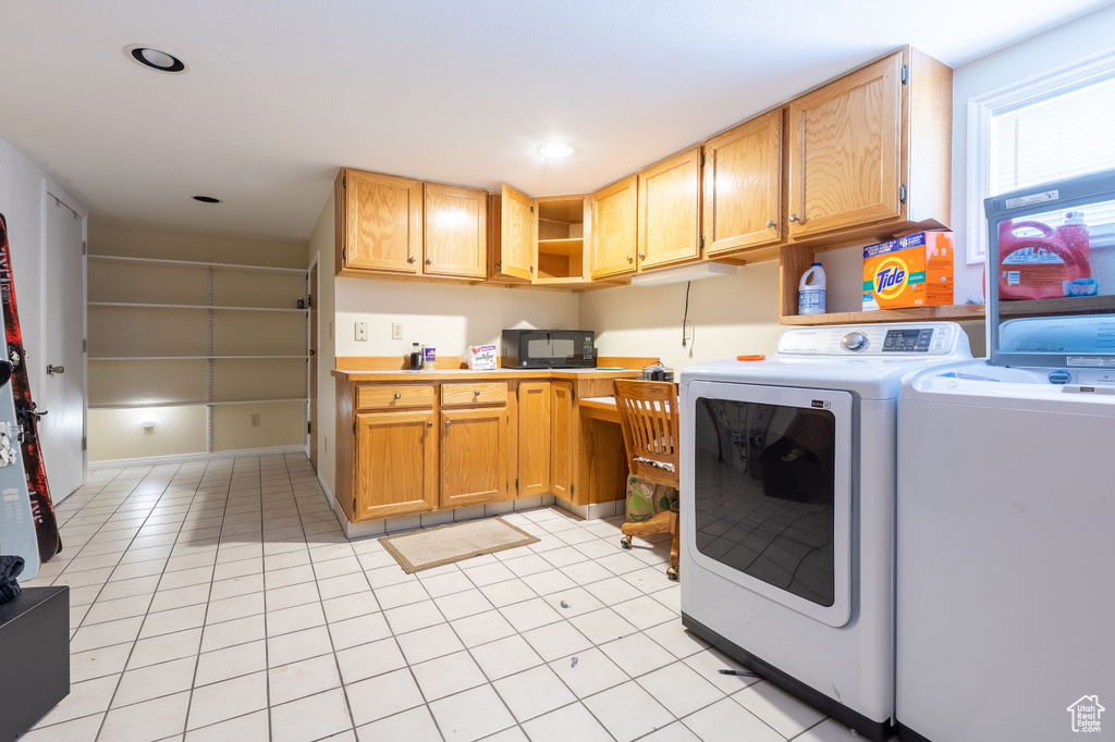 Clothes washing area with light tile flooring, washer and dryer, and cabinets