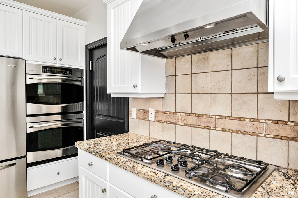 Kitchen featuring backsplash, stainless steel appliances, light stone counters, and wall chimney range hood