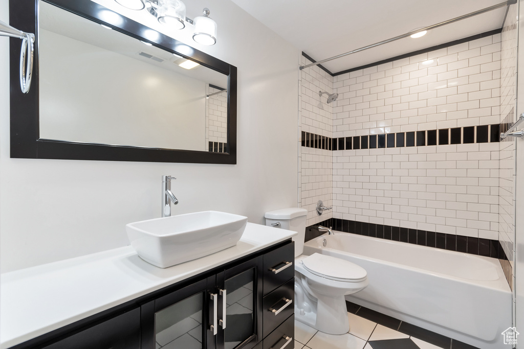 Full bathroom with toilet, tiled shower / bath combo, oversized vanity, and tile floors