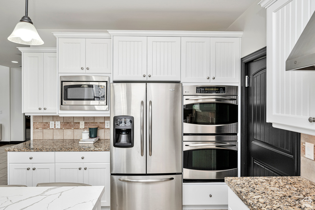 Kitchen featuring white cabinets, stainless steel appliances, light stone counters, and tasteful backsplash