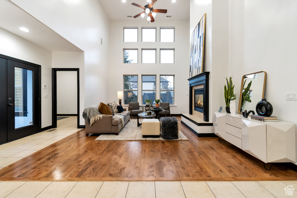 Living room featuring light tile flooring, a towering ceiling, ceiling fan, and a tile fireplace