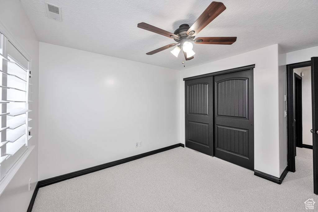 Unfurnished bedroom featuring light colored carpet, a textured ceiling, ceiling fan, and a closet