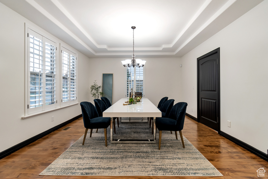 Dining space with a chandelier, a raised ceiling, and dark hardwood / wood-style floors