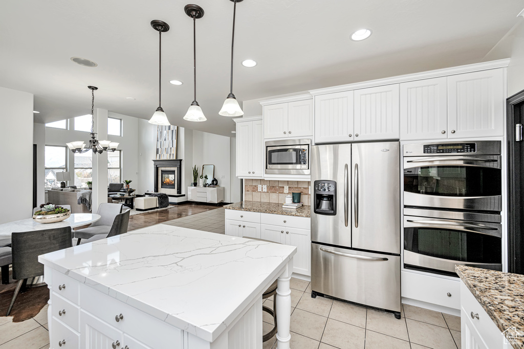 Kitchen featuring light stone countertops, appliances with stainless steel finishes, backsplash, white cabinets, and pendant lighting