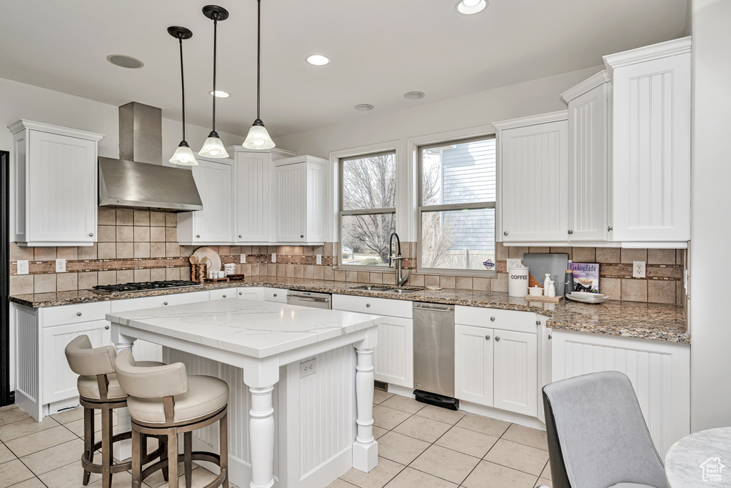 Kitchen featuring white cabinetry, backsplash, light stone countertops, and wall chimney range hood