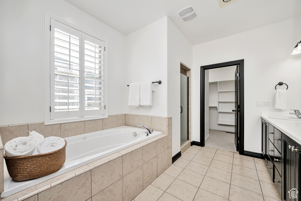 Bathroom with tile flooring, plenty of natural light, tiled tub, and vanity