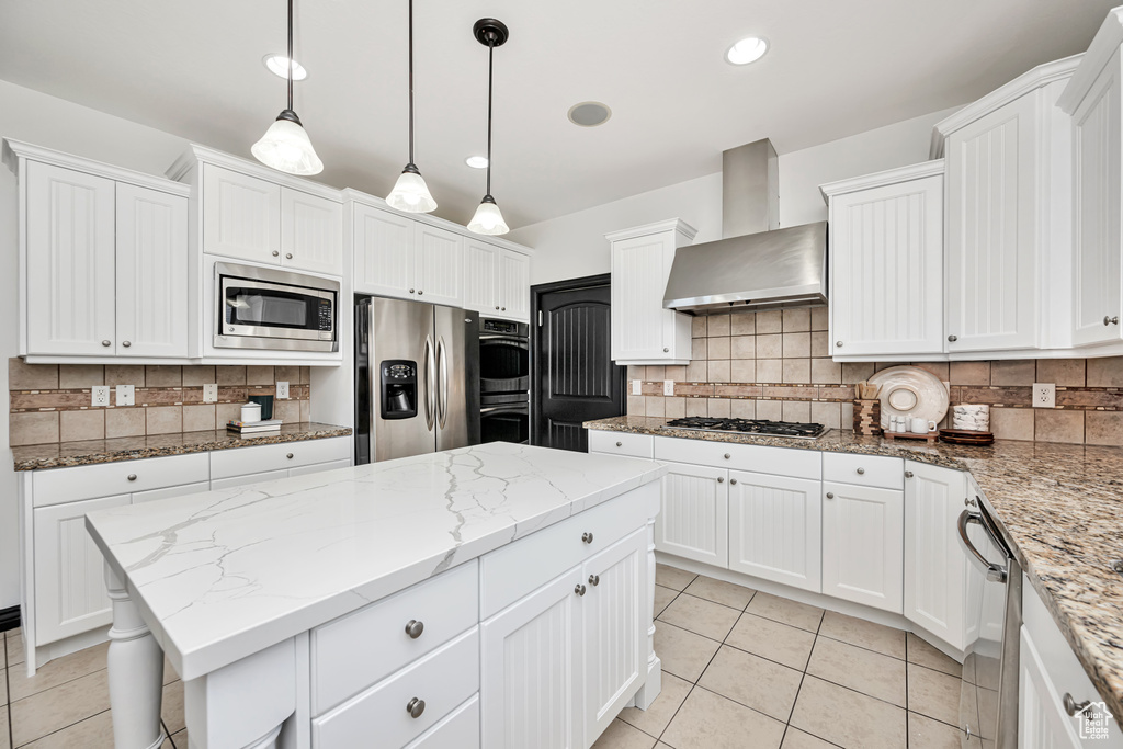 Kitchen with wall chimney exhaust hood, white cabinets, stainless steel appliances, and backsplash