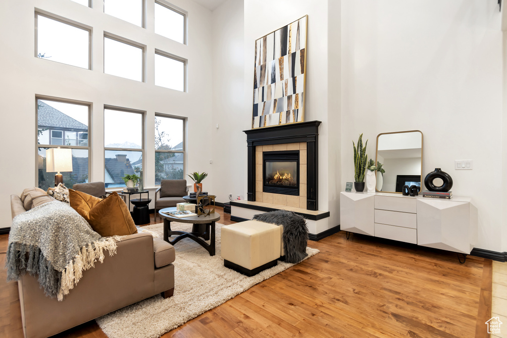 Living room featuring a towering ceiling, a tiled fireplace, and light hardwood / wood-style floors