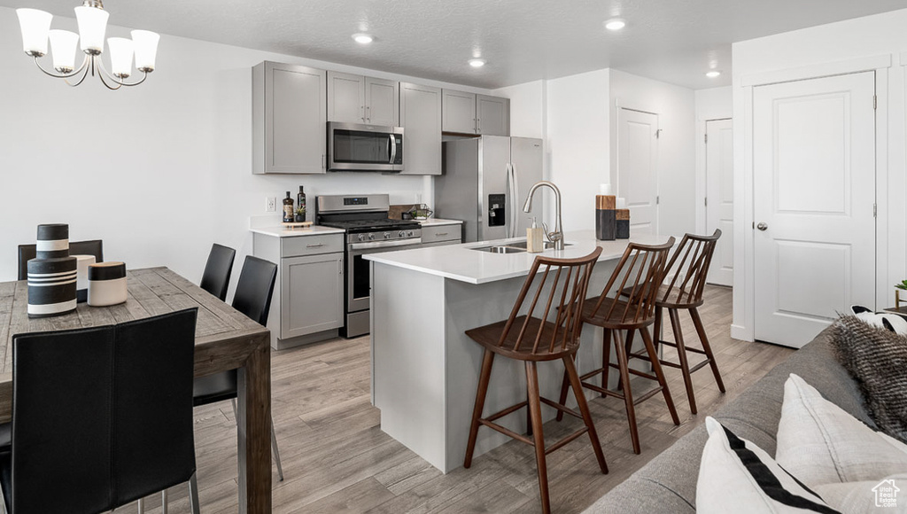 Kitchen with a notable chandelier, gray cabinets, light hardwood / wood-style floors, appliances with stainless steel finishes, and a breakfast bar area
