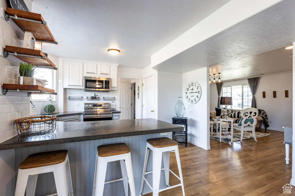 Kitchen featuring tasteful backsplash, a kitchen bar, dark wood-type flooring, appliances with stainless steel finishes, and white cabinets