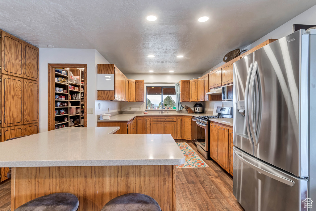 Kitchen with hardwood / wood-style flooring, a textured ceiling, stainless steel appliances, sink, and a breakfast bar area