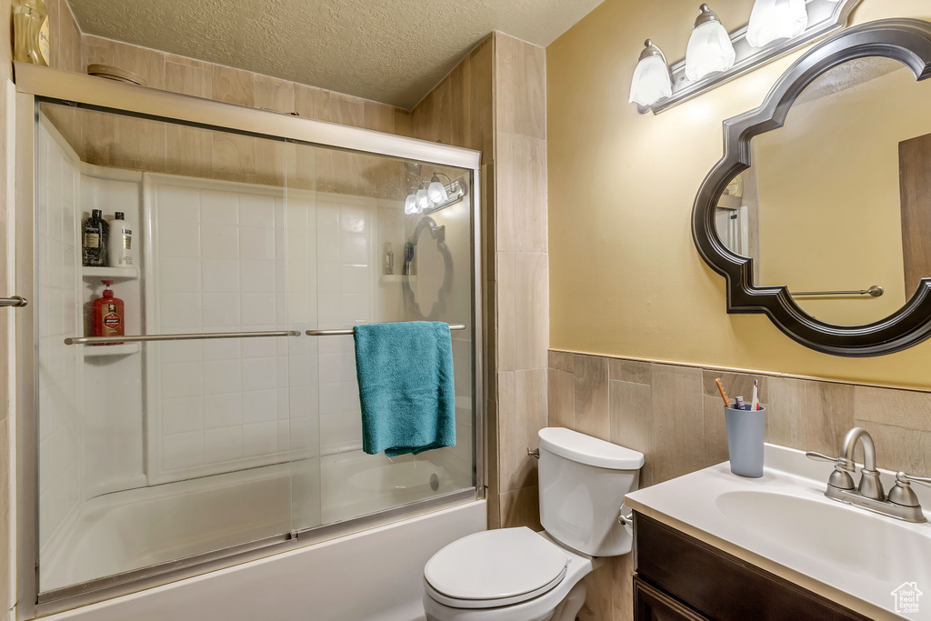 Full bathroom with bath / shower combo with glass door, tile walls, backsplash, toilet, and vanity