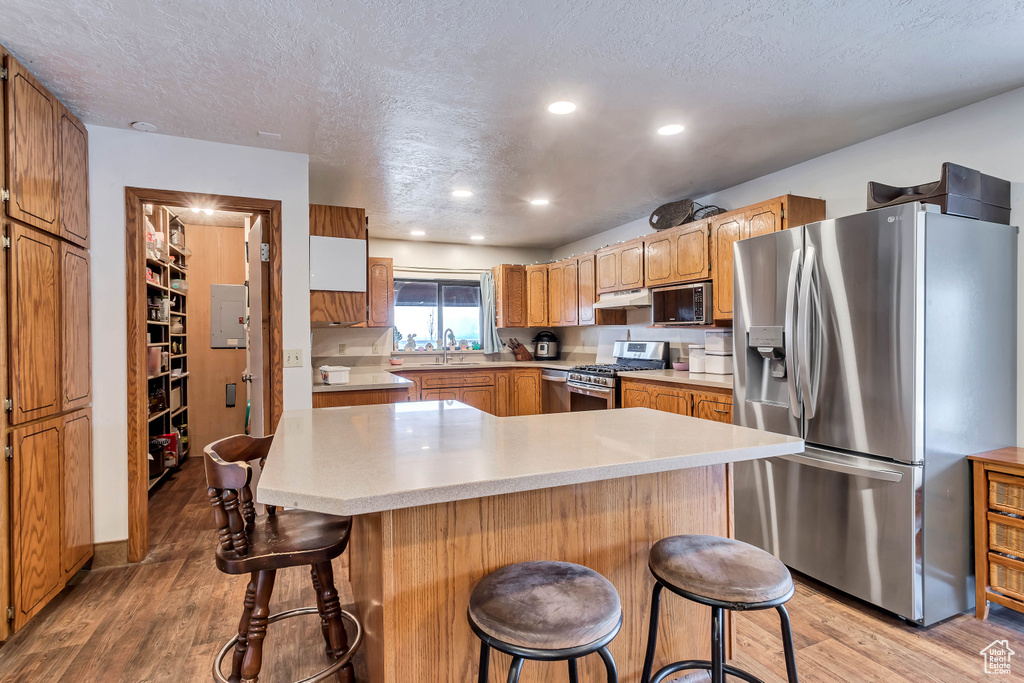 Kitchen with appliances with stainless steel finishes, hardwood / wood-style floors, sink, and a kitchen bar