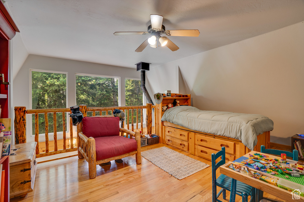 Bedroom with a wood stove, light hardwood / wood-style floors, and ceiling fan
