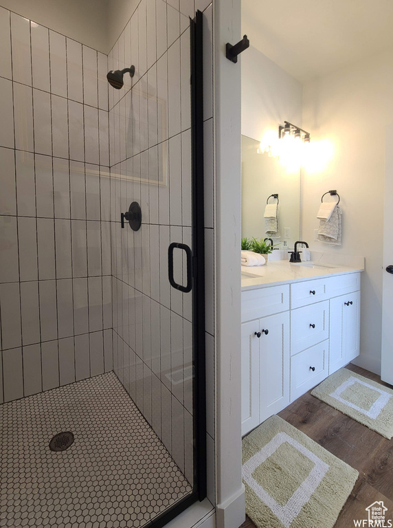 Bathroom with double sink vanity, wood-type flooring, and a shower with door