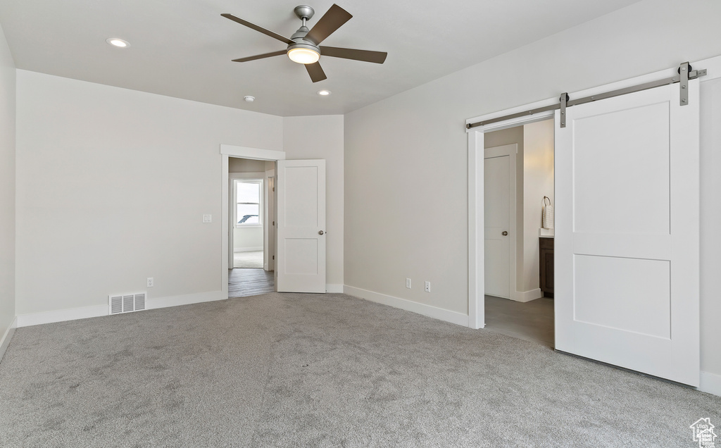 Unfurnished bedroom featuring light carpet, a barn door, and ceiling fan