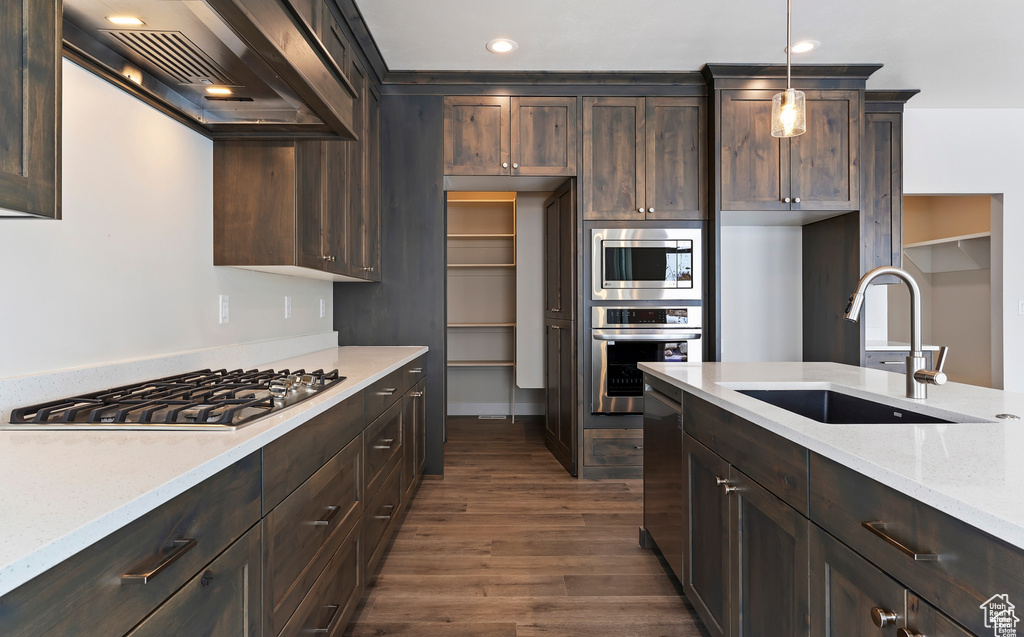 Kitchen featuring dark hardwood / wood-style floors, custom exhaust hood, appliances with stainless steel finishes, light stone counters, and pendant lighting