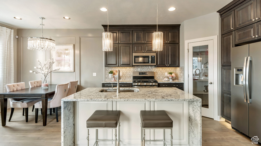 Kitchen with tasteful backsplash, appliances with stainless steel finishes, an inviting chandelier, light stone countertops, and a kitchen bar