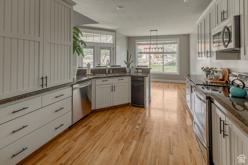 Kitchen featuring light hardwood / wood-style flooring, hanging light fixtures, white cabinetry, sink, and appliances with stainless steel finishes
