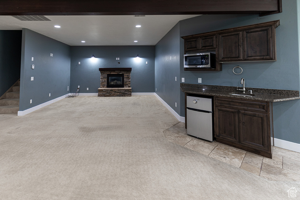 Kitchen featuring dark stone counters, a stone fireplace, light colored carpet, sink, and stainless steel microwave