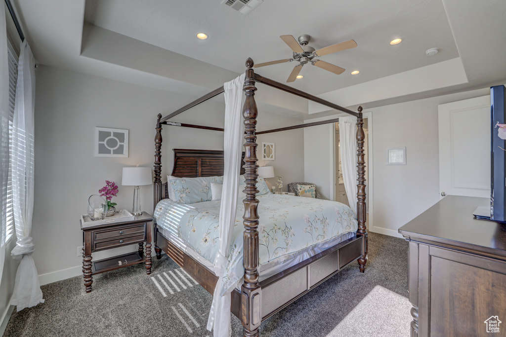 Bedroom with dark carpet, a tray ceiling, and ceiling fan