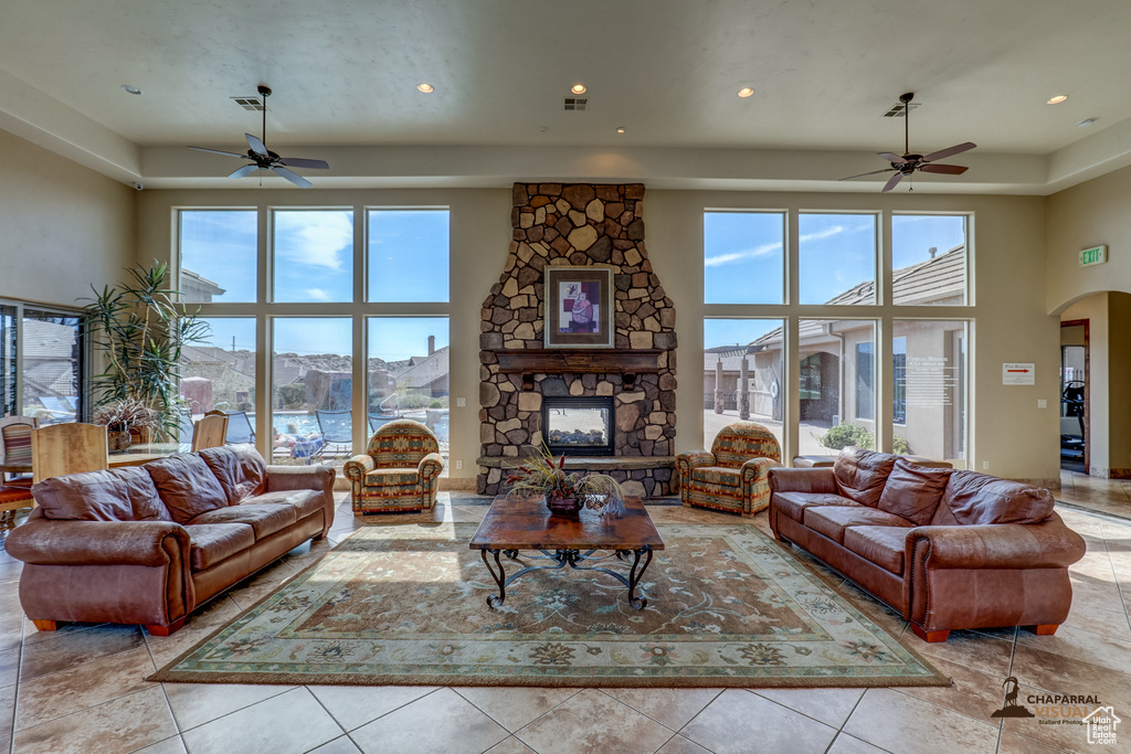 Tiled living room with ceiling fan, a stone fireplace, and a high ceiling