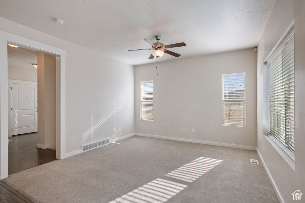 Empty room with a textured ceiling, dark colored carpet, and ceiling fan