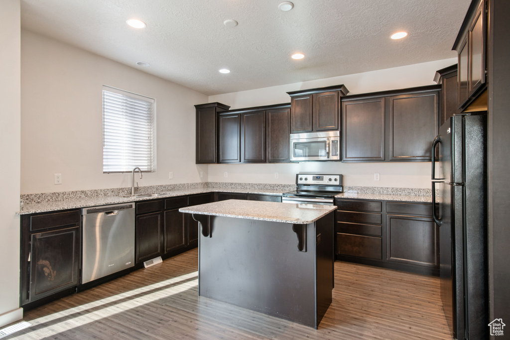 Kitchen with sink, dark hardwood / wood-style flooring, a kitchen island, stainless steel appliances, and a breakfast bar area