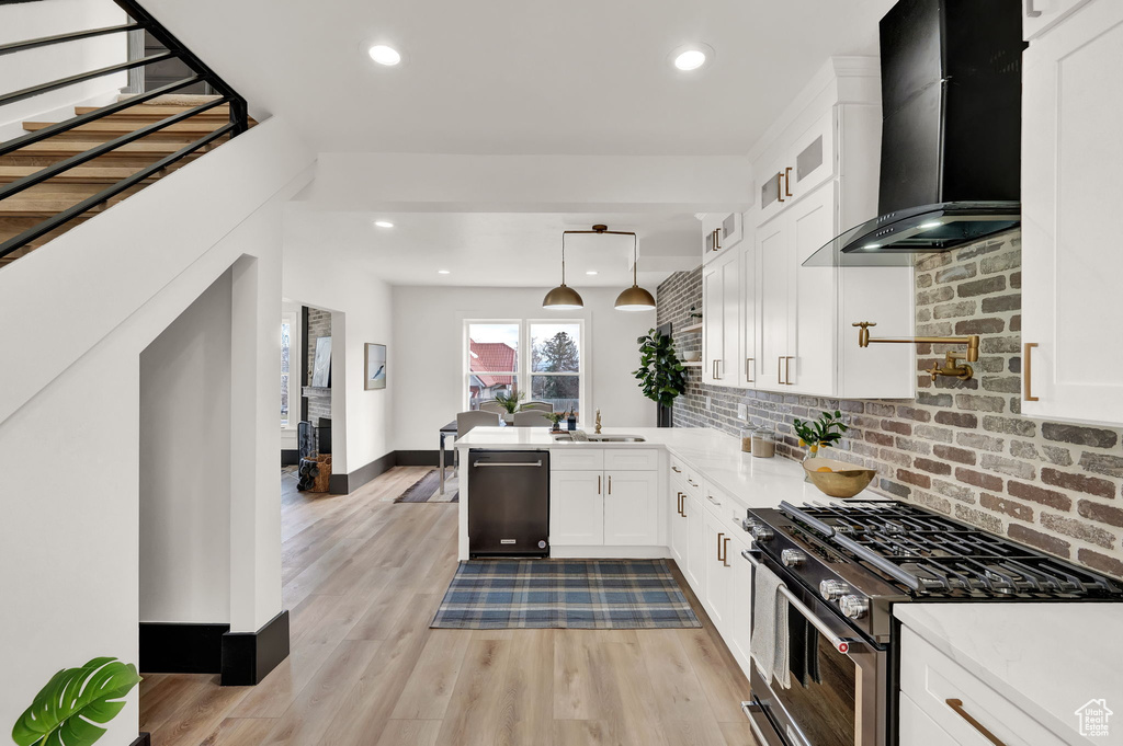 Kitchen with wall chimney range hood, tasteful backsplash, dishwasher, high end stainless steel range, and white cabinetry