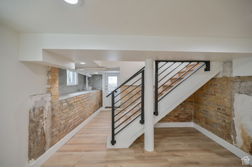 Stairs with light hardwood / wood-style floors and brick wall