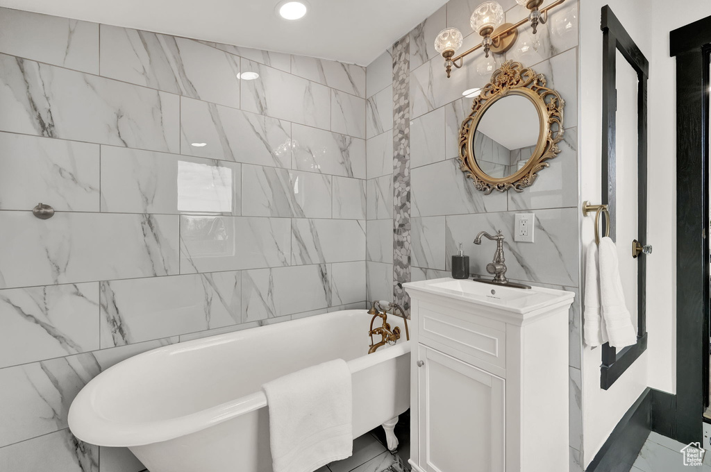 Bathroom featuring tile flooring, vanity with extensive cabinet space, tile walls, and a tub