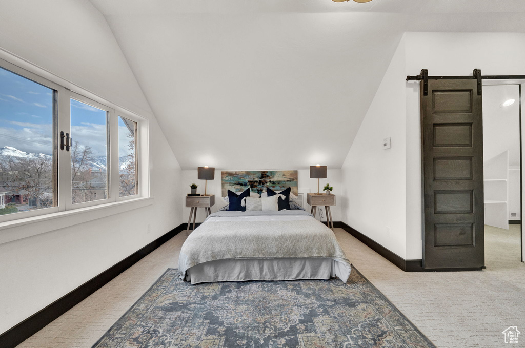 Bedroom featuring a barn door, lofted ceiling, and light colored carpet