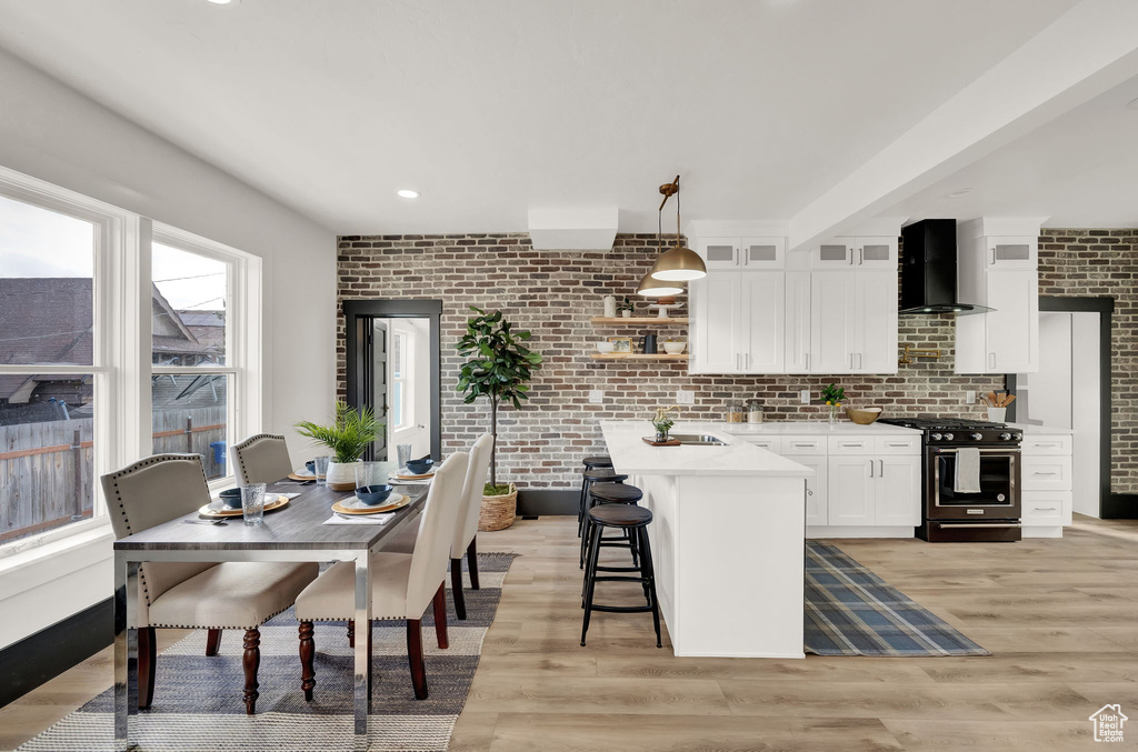 Kitchen with white cabinets, wall chimney range hood, pendant lighting, light hardwood / wood-style floors, and high end black range