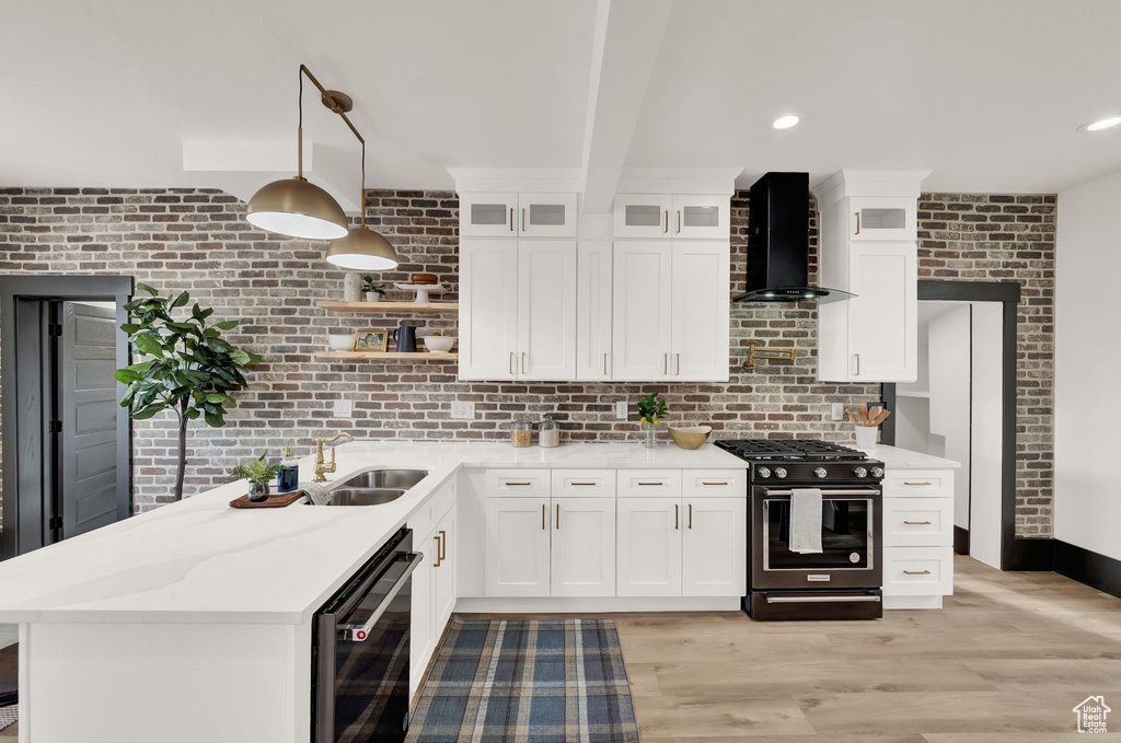 Kitchen featuring white cabinets, wall chimney range hood, gas stove, and hanging light fixtures