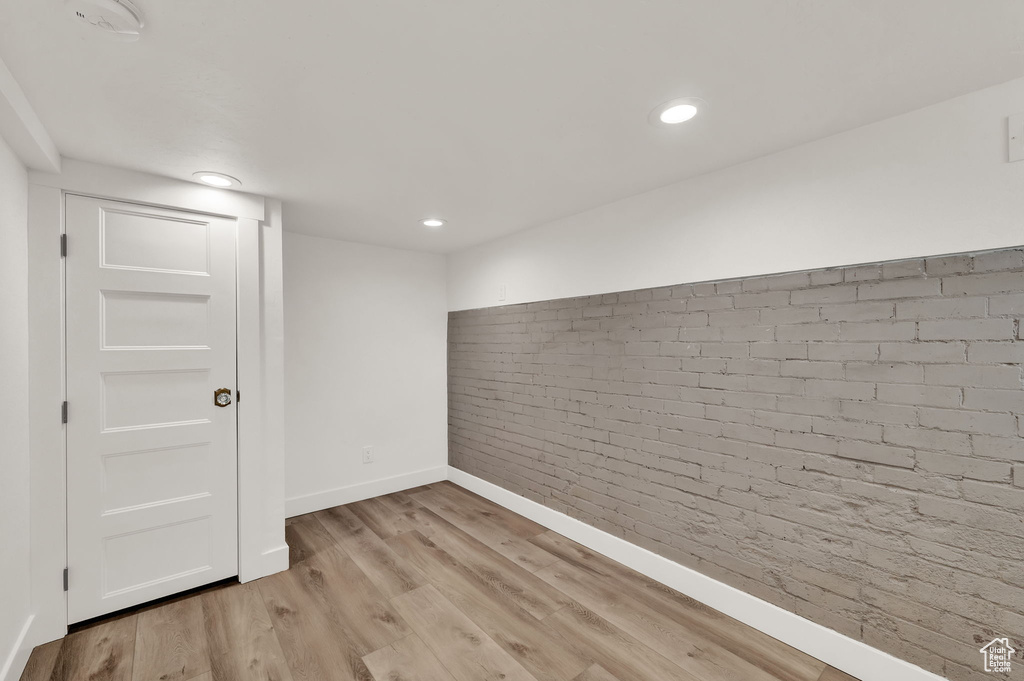 Basement featuring brick wall and light hardwood / wood-style flooring