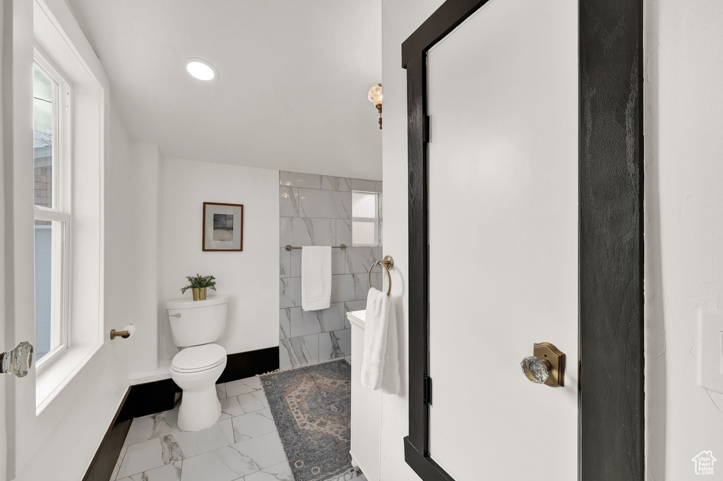 Bathroom with a wealth of natural light, toilet, tile walls, and tile floors