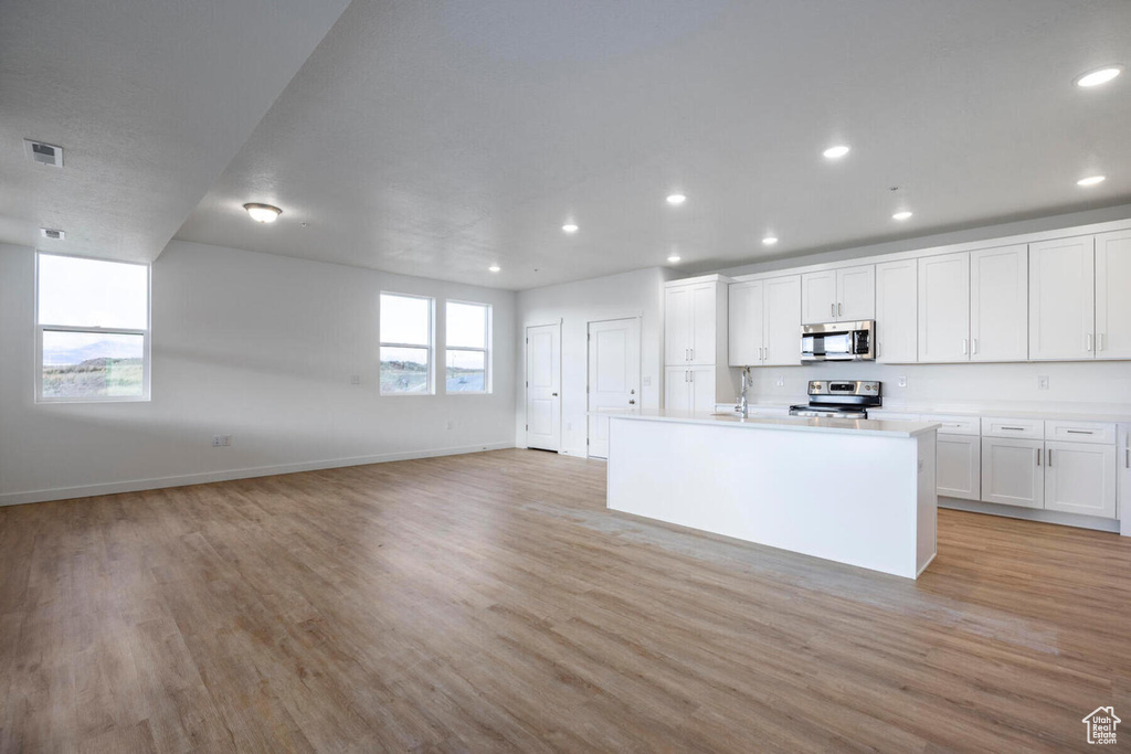 Kitchen with white cabinetry, light hardwood / wood-style flooring, stainless steel appliances, and a center island with sink