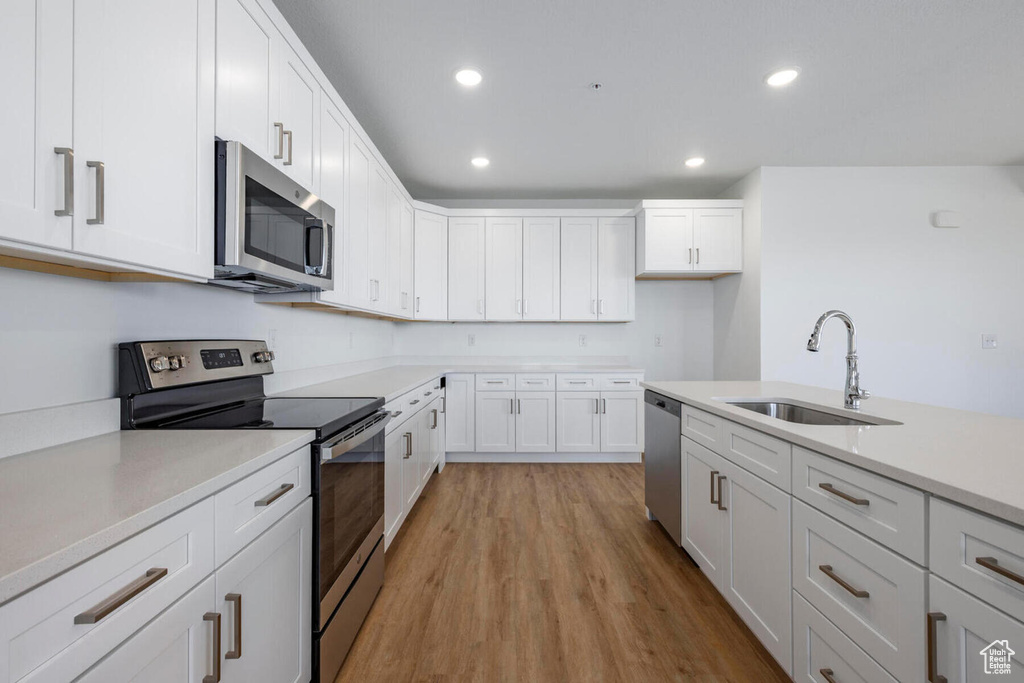 Kitchen with appliances with stainless steel finishes, white cabinetry, light hardwood / wood-style floors, and sink
