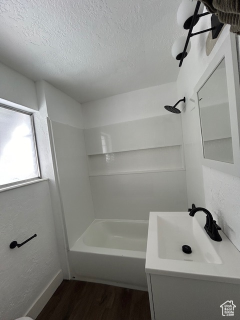 Bathroom with a textured ceiling, large vanity, washtub / shower combination, and wood-type flooring