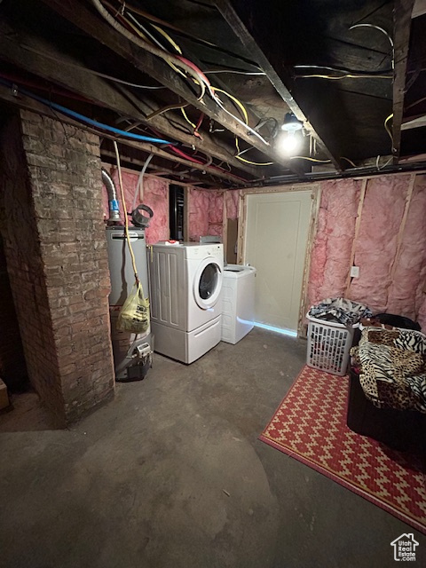 Basement with brick wall, water heater, and washer and dryer