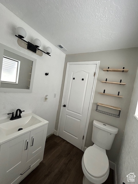 Bathroom with a textured ceiling, hardwood / wood-style floors, toilet, and vanity