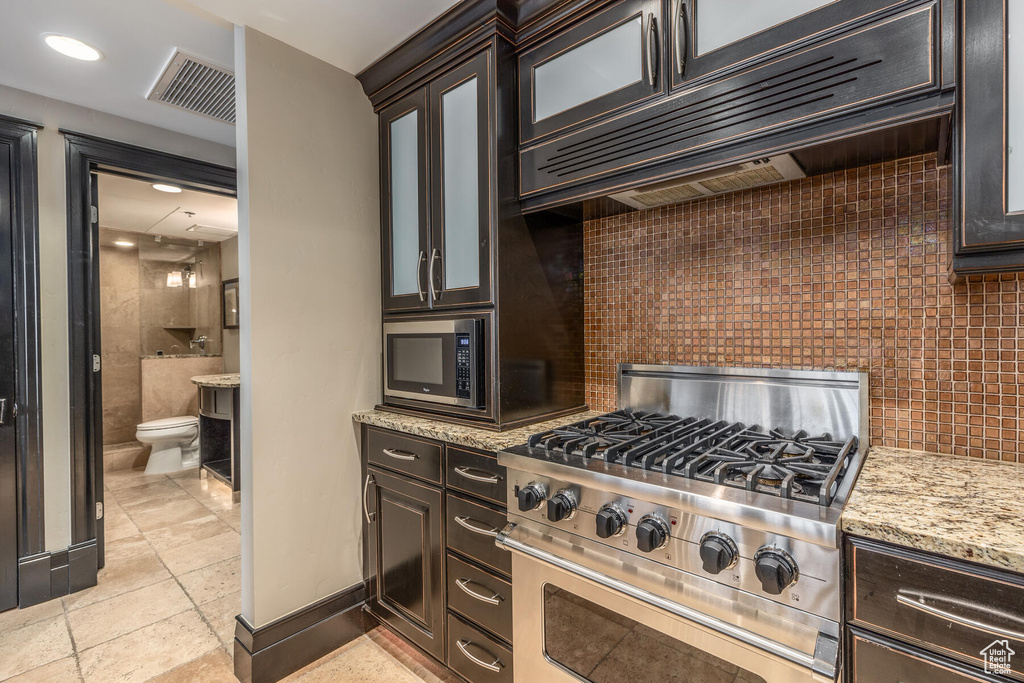 Kitchen with light tile flooring, stainless steel range, built in microwave, premium range hood, and dark brown cabinets