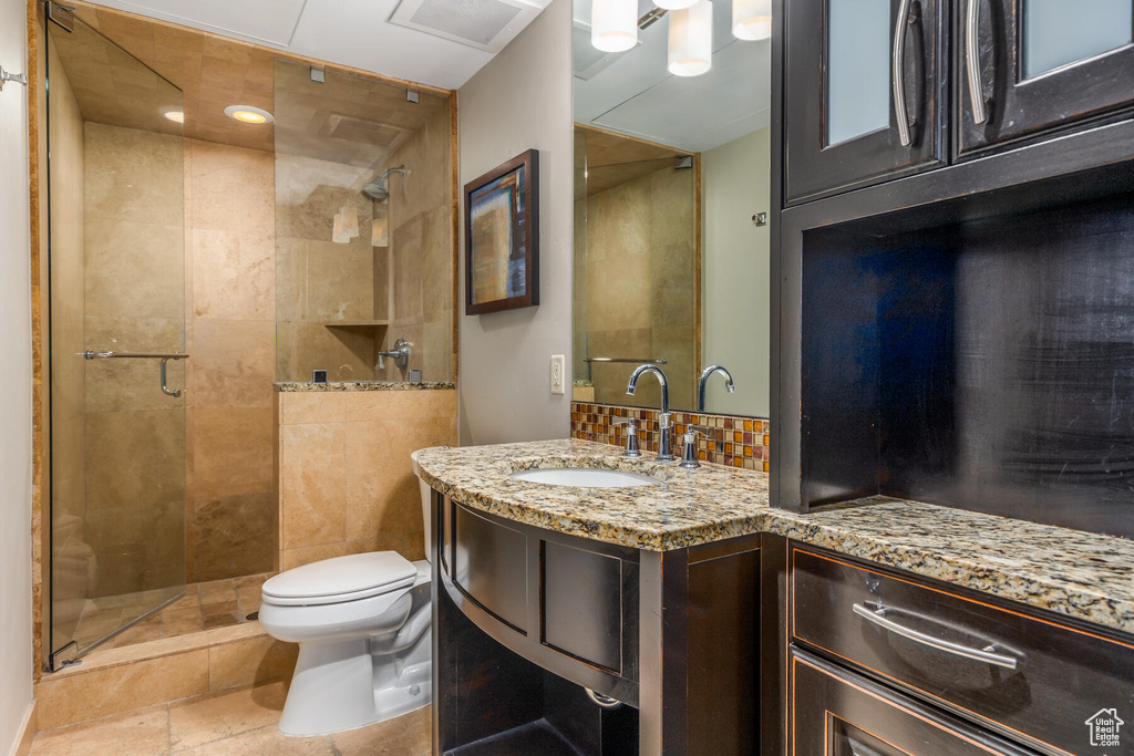 Bathroom featuring toilet, a tile shower, vanity with extensive cabinet space, and tile floors