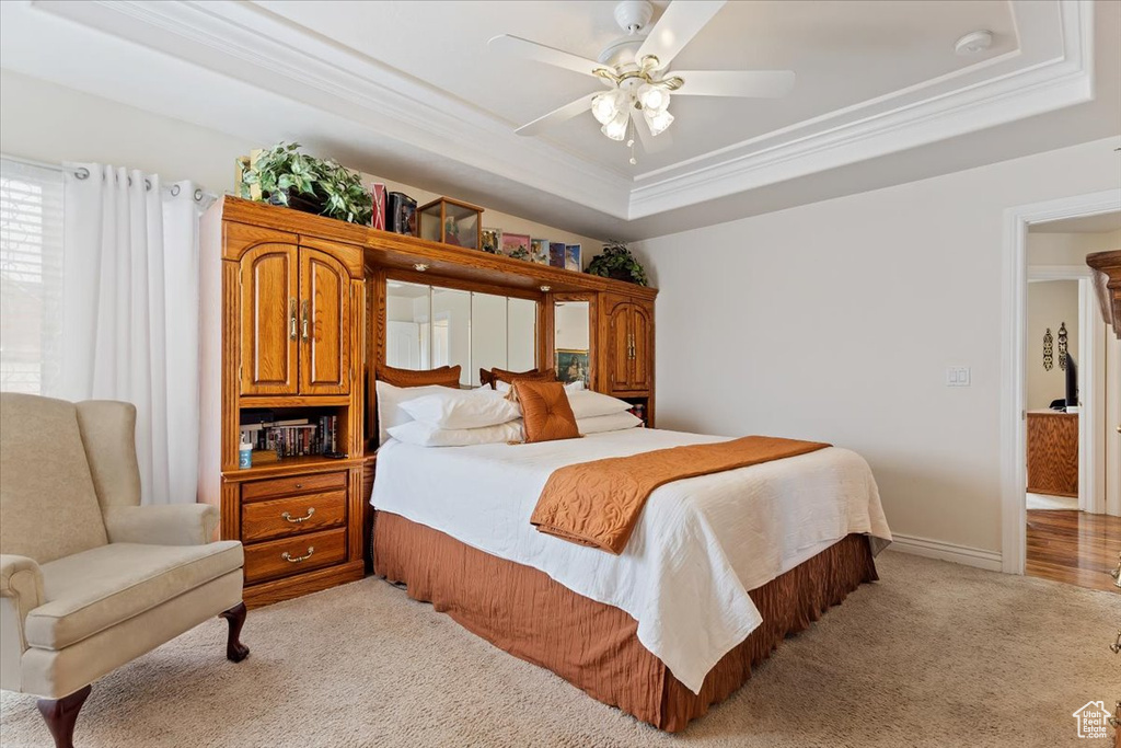 Carpeted bedroom featuring a tray ceiling, crown molding, and ceiling fan
