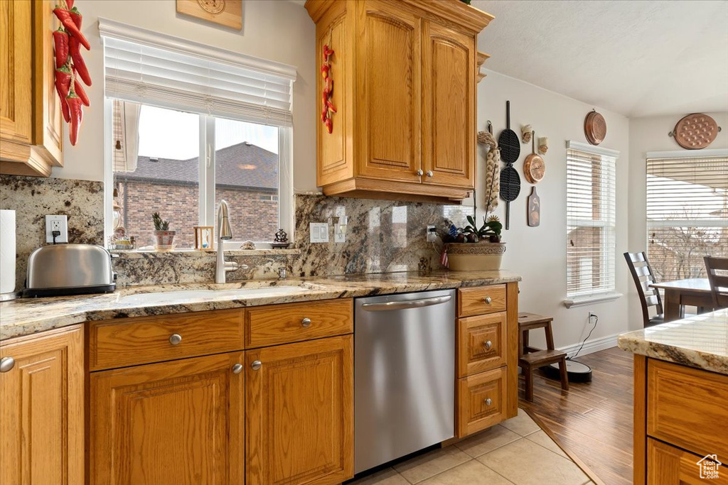 Kitchen with stainless steel dishwasher, light tile floors, light stone countertops, and backsplash