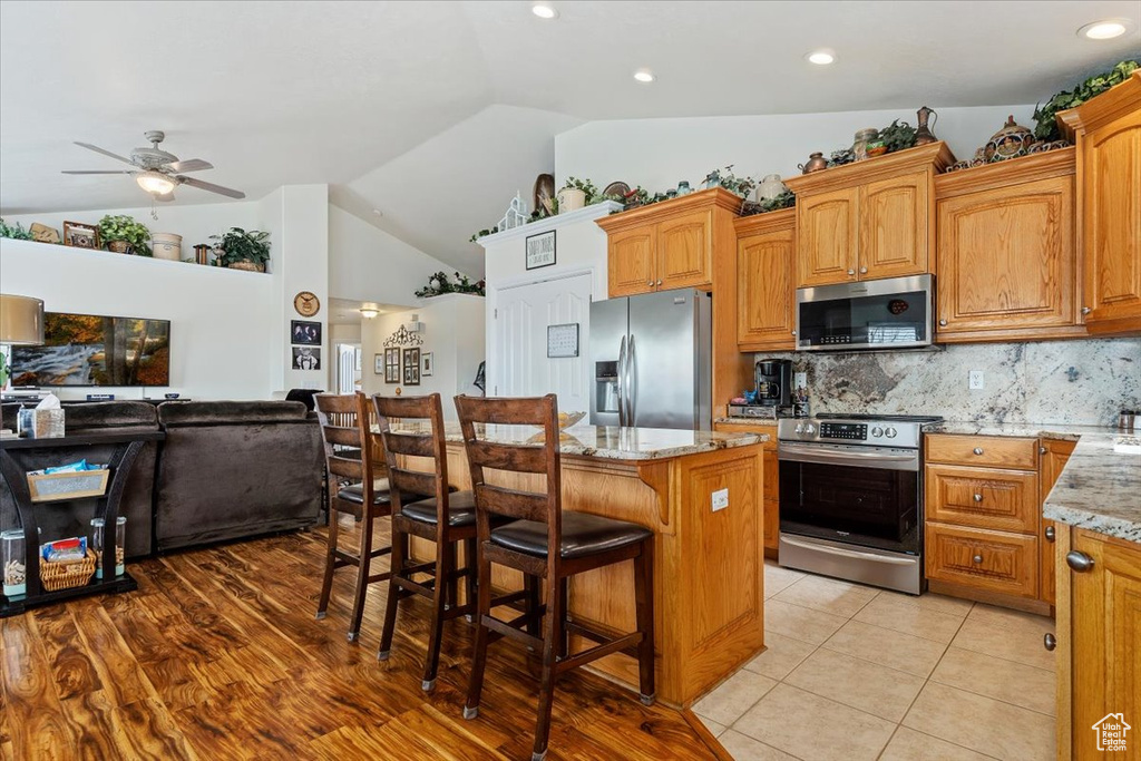 Kitchen featuring backsplash, stainless steel appliances, ceiling fan, light stone counters, and a center island