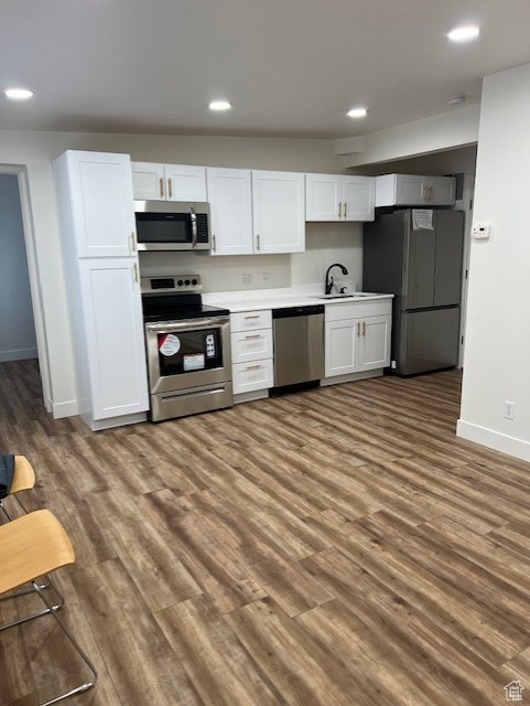 Kitchen with dark wood-type flooring, white cabinets, appliances with stainless steel finishes, and sink