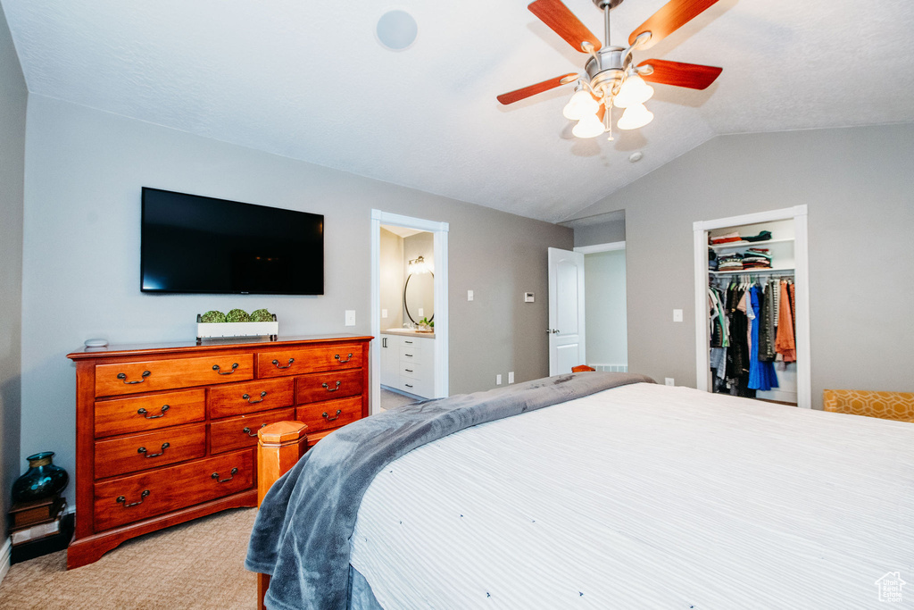 Carpeted bedroom with a spacious closet, connected bathroom, lofted ceiling, a closet, and ceiling fan