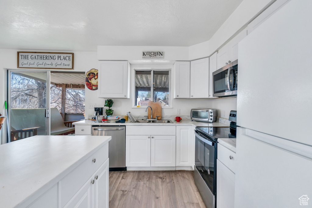 Kitchen with appliances with stainless steel finishes, white cabinetry, sink, and light wood-type flooring