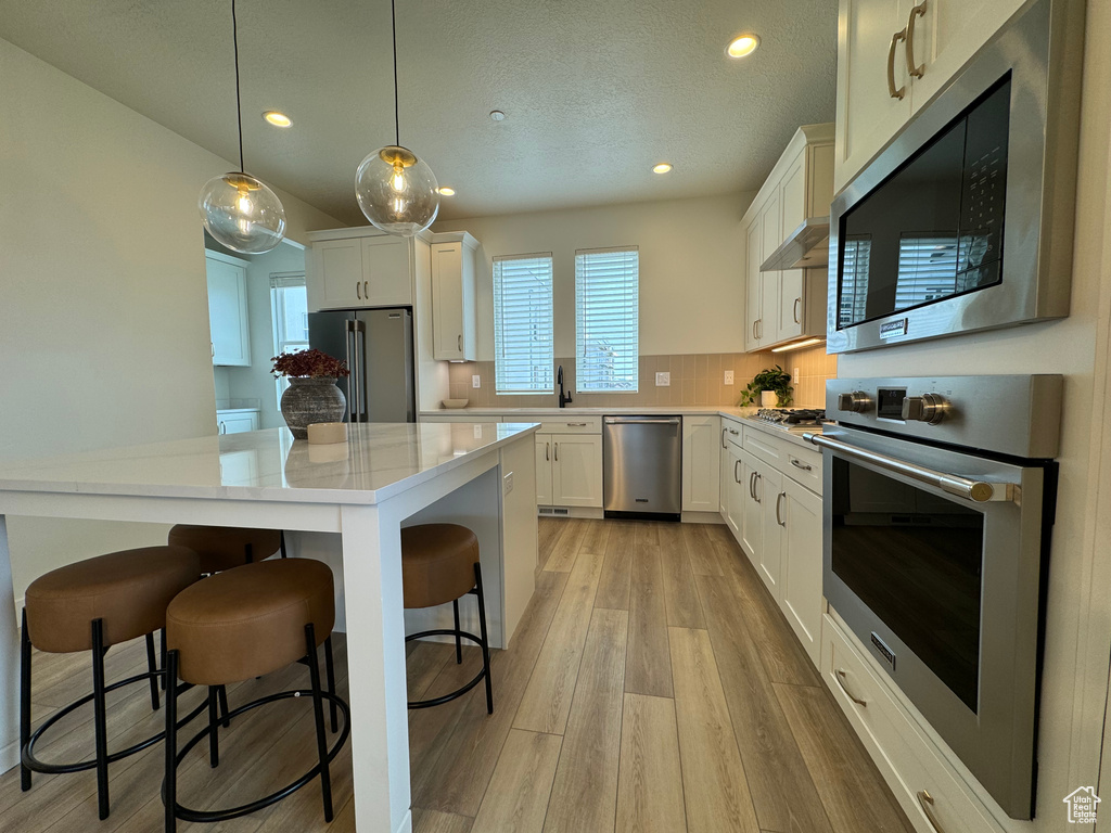 Kitchen with white cabinets, stainless steel appliances, a breakfast bar area, light hardwood / wood-style flooring, and pendant lighting